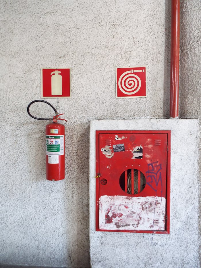 Red fire extinguisher and hose cabinet on a textured concrete wall in a safety setup.
